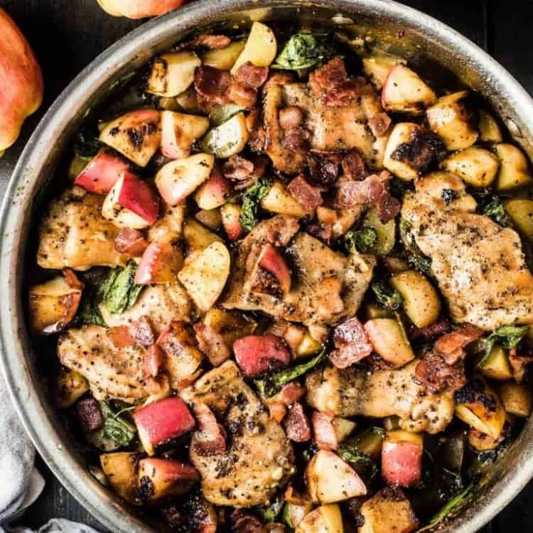 Looking down on a pan of this apple chicken recipe on a black table with apples on the side.