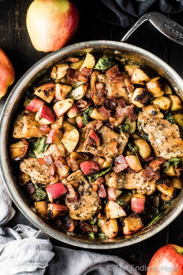 Looking down on a pan of this apple chicken recipe on a black table with apples on the side. 