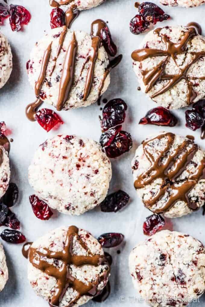 A tray of Cranberry Coconut Macaroons with chocolate drizzled on top and cranberries on the side.
