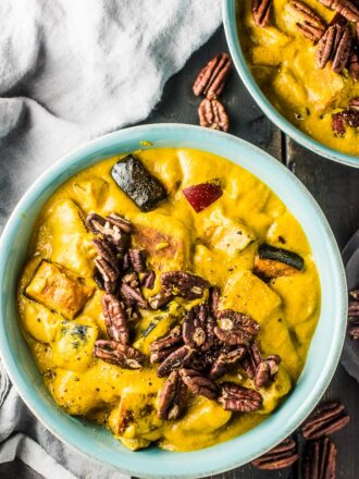 A blue bowl filled with bright yellow pumpkin curry with apples topped with toasted pecans. .