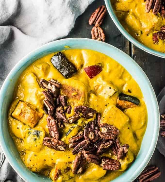 A blue bowl filled with bright yellow pumpkin curry with apples topped with toasted pecans. .