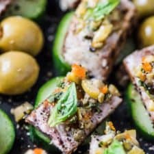 A platter of seared tuna bites on cucumber rounds with olive tapenade on top and manzanilla olives from spain on the side.