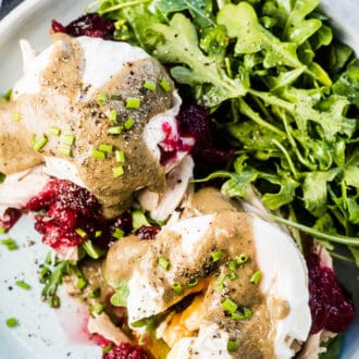 Thanksgiving Leftover Turkey Eggs Benedict with cranberry sauce and gravy on a plate with an arugula salad on the side.