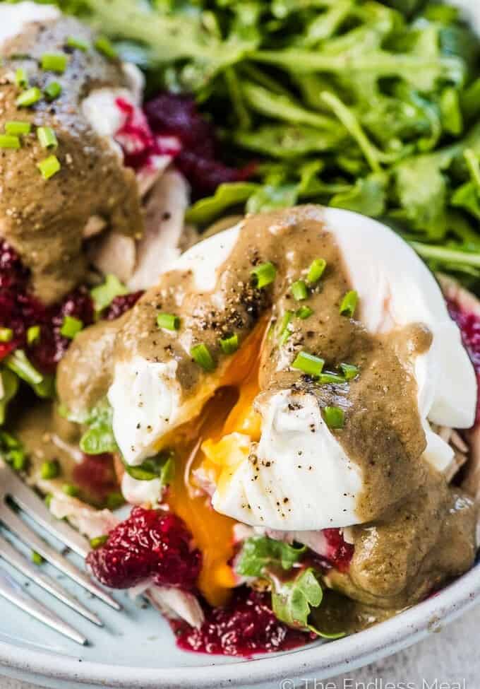 A close up of Thanksgiving Leftover Turkey Eggs Benedict with cranberry sauce and gravy on a plate with an arugula salad on the side.