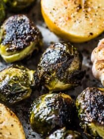 A close up of whole roasted brussels sprouts with garlic and lemon on a baking tray.