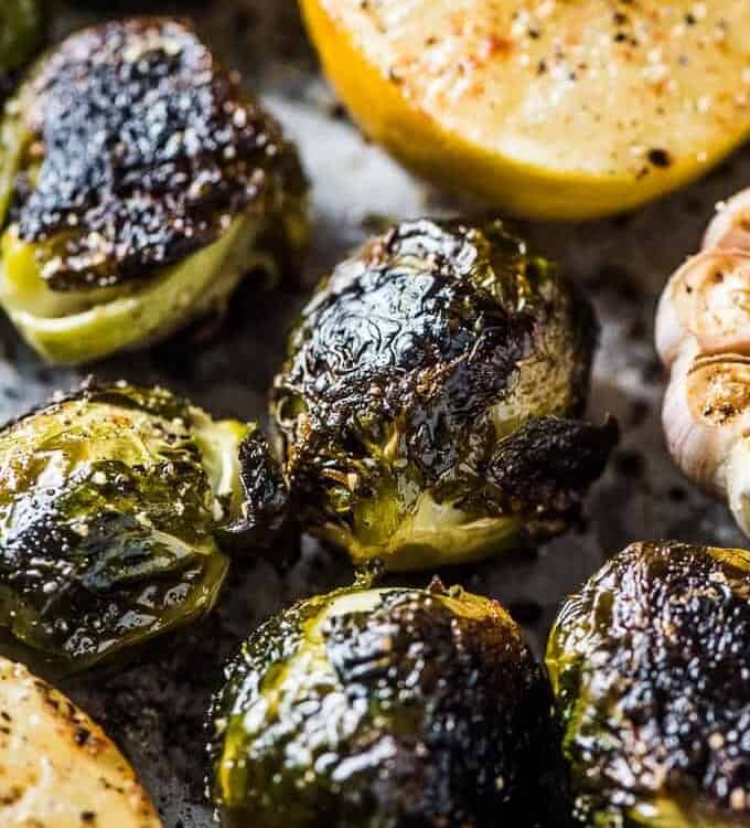 A close up of whole roasted brussels sprouts with garlic and lemon on a baking tray.