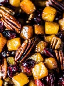 A close up of maple roasted butternut squash with cranberries and pecans on a baking sheet.