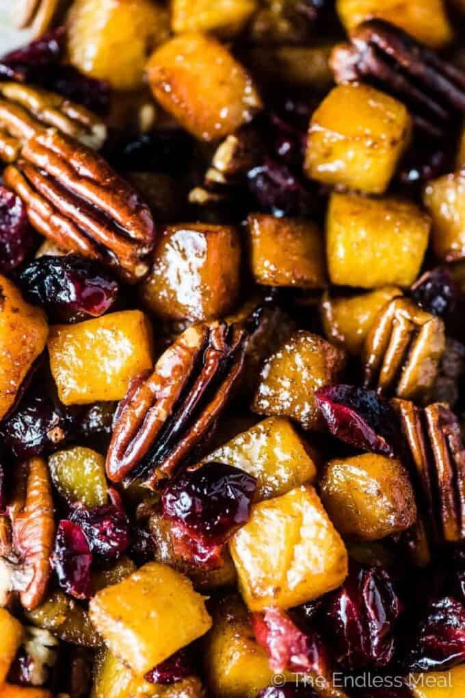 A close up of maple roasted butternut squash with cranberries and pecans on a baking sheet.