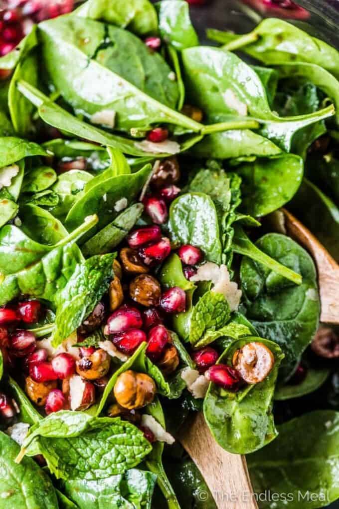 A close up of this spinach pomegranate salad with lots of pomegranates and hazelnuts.