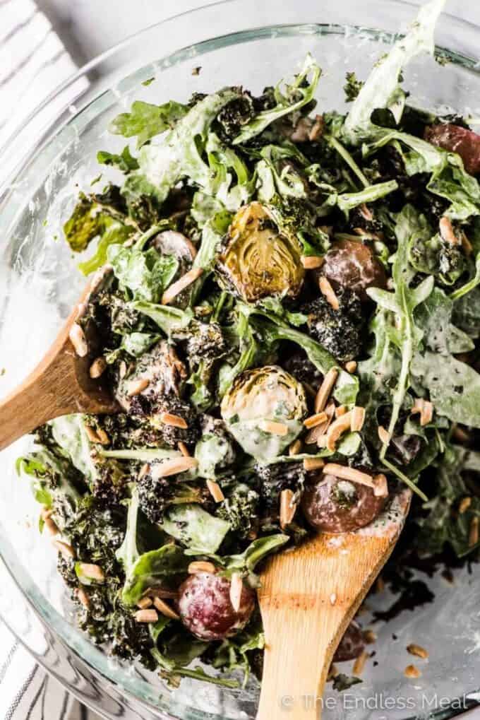 Roasted winter green salad in a glass bowl with wooden salad serving spoons in it.