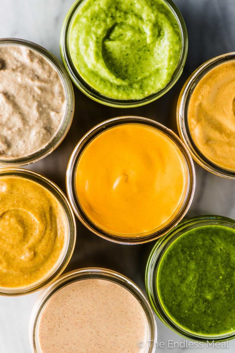 A closeup of 7 Whole30 sauces in glass jars on a marble table.