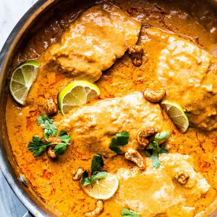 coconut salmon curry in a pan with limes and cashews.