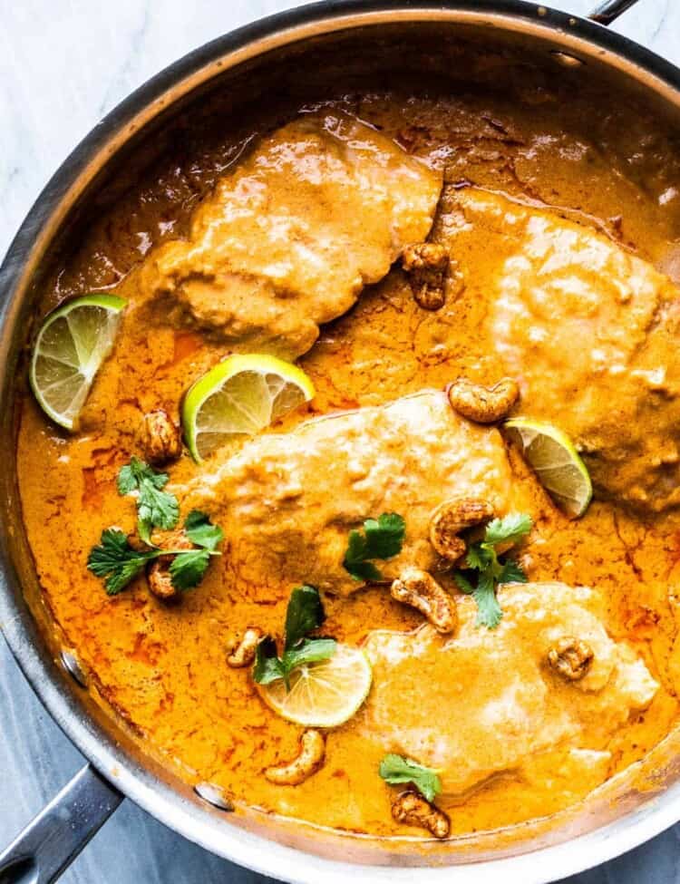 coconut salmon curry in a pan with limes and cashews.