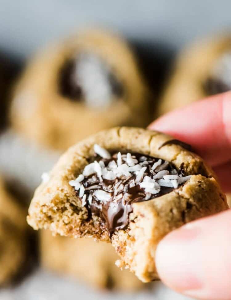 A hand holding a Chocolate Almond Thumbprint Cookies with a bite taken out of it.