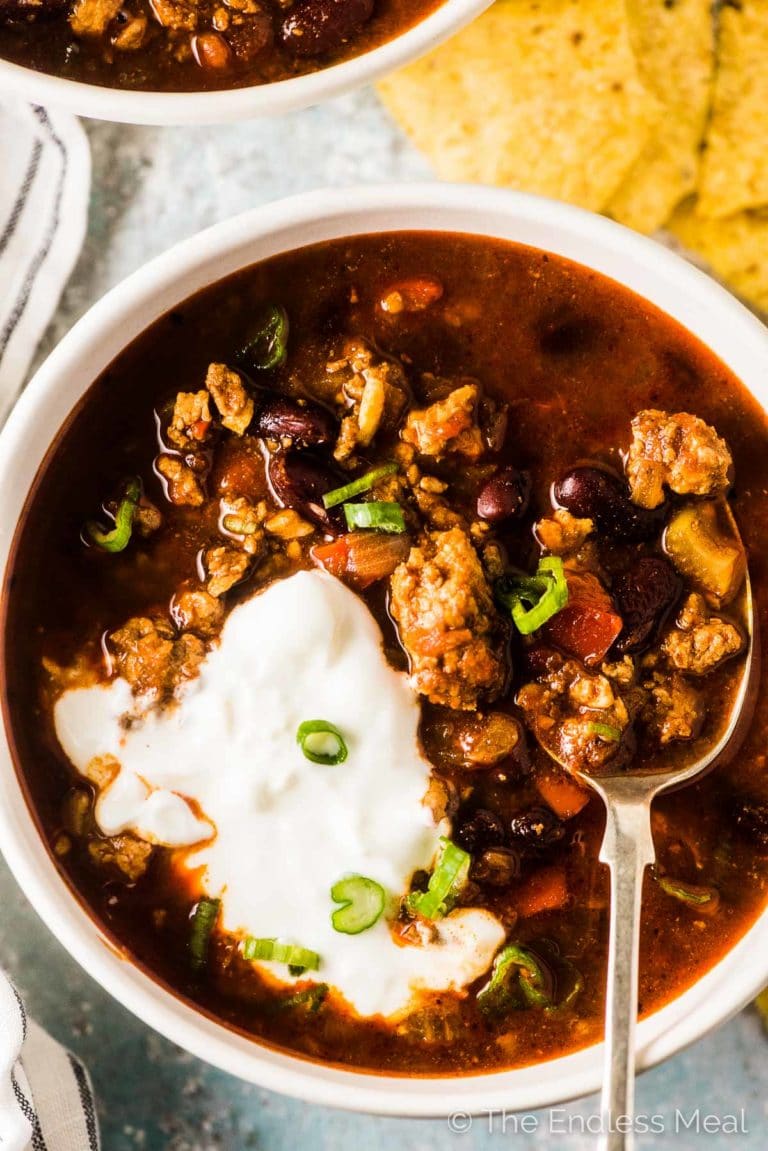A bowl of this turkey chili recipe with some sour cream and green onions and a spoon in the bowl.