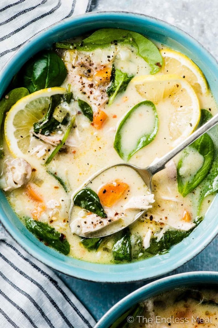 A blue bowl filled with lemon chicken soup with a spoon in it. 