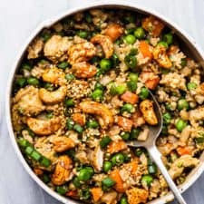A bowl of cauliflower rice with carrots, peas, and cashews.