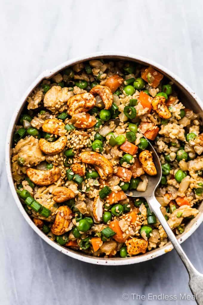 A bowl of cauliflower rice with carrots, peas, and cashews.