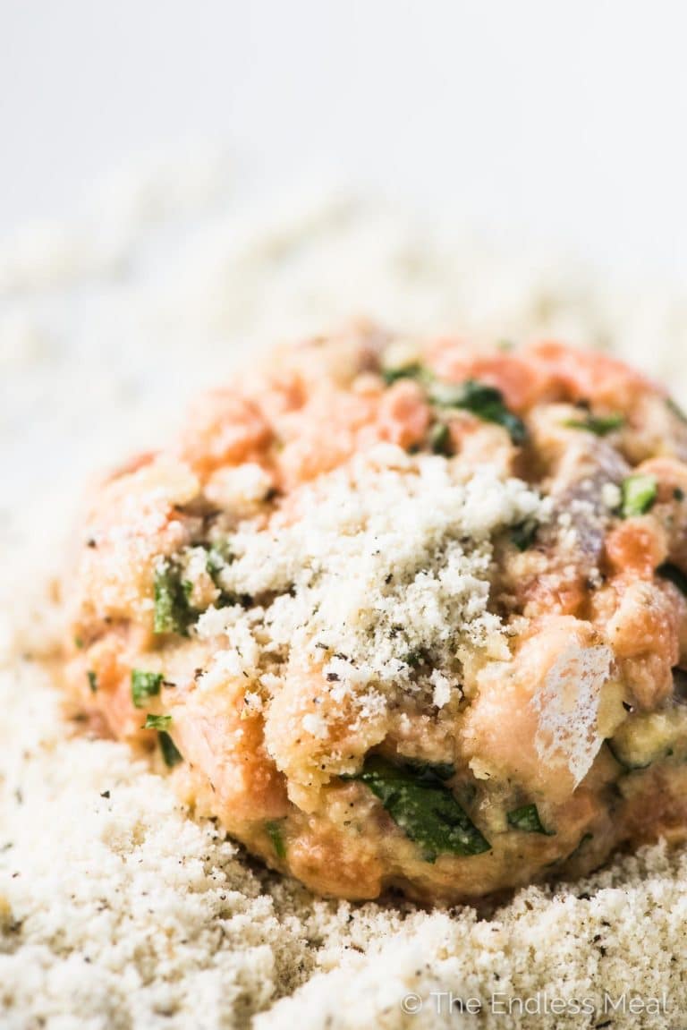 A raw salmon cake in a bowl of almond flour with a little almond flour on top. 