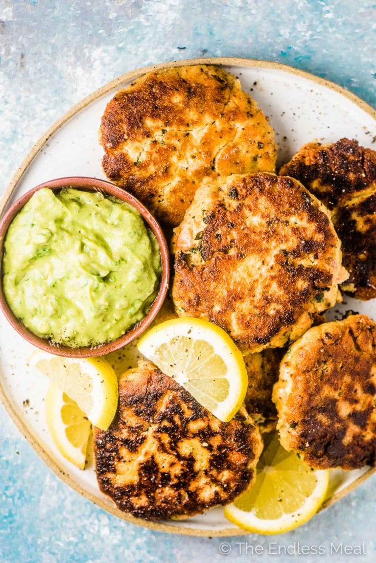 All the fish cakes from this salmon cakes recipe on a white plate with lemons and avocado tartare sauce on the side. 