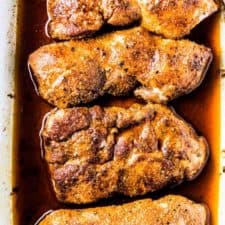 4 juicy baked pork chops in a white baking dish.