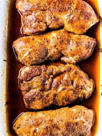 4 juicy baked pork chops in a white baking dish.