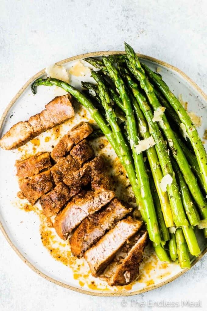 AN oven baked pork chop on a dinner plate with asparagus.