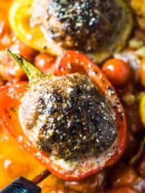 A close up of a giant meatball stuffed pepper in a casserole dish with cherry tomatoes.