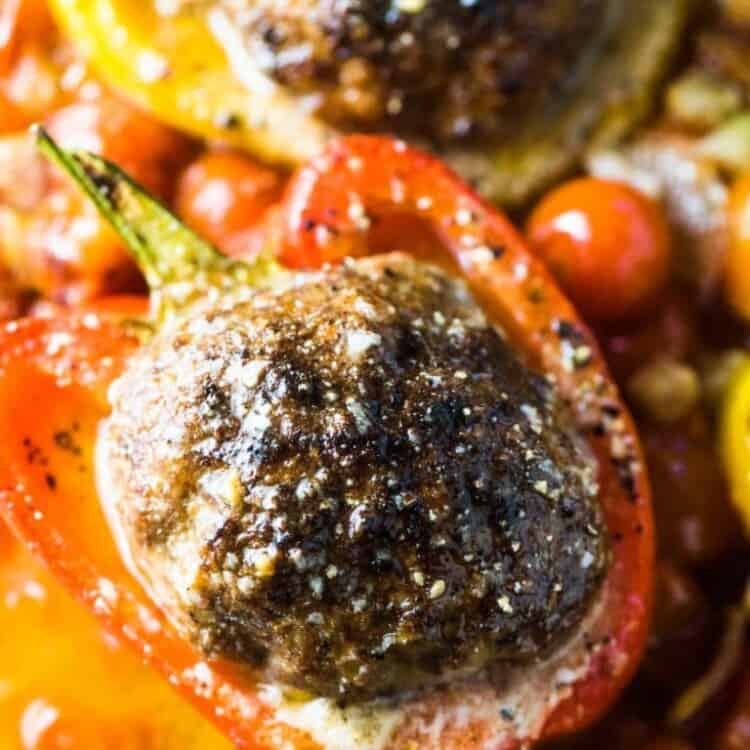 A close up of a giant meatball stuffed pepper in a casserole dish with cherry tomatoes.