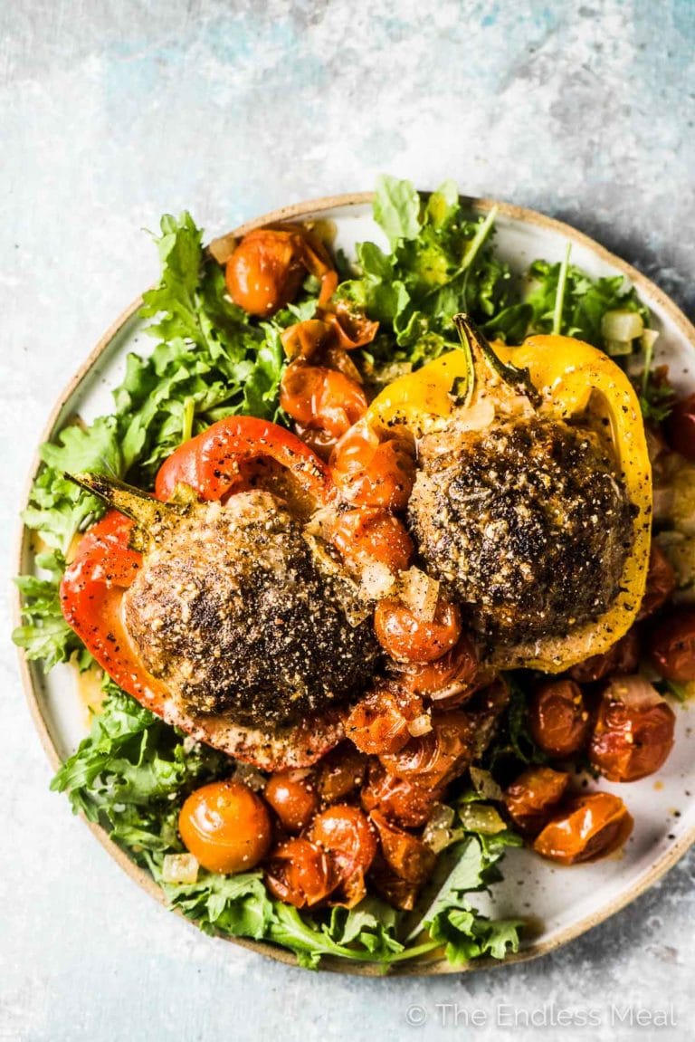 2 meatball stuffed peppers in a plate with baby kale and the cherry tomato sauce poured over the top. 