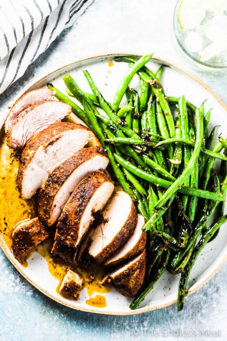 A perfect baked chicken breast cut into slices on a plate with green beans.