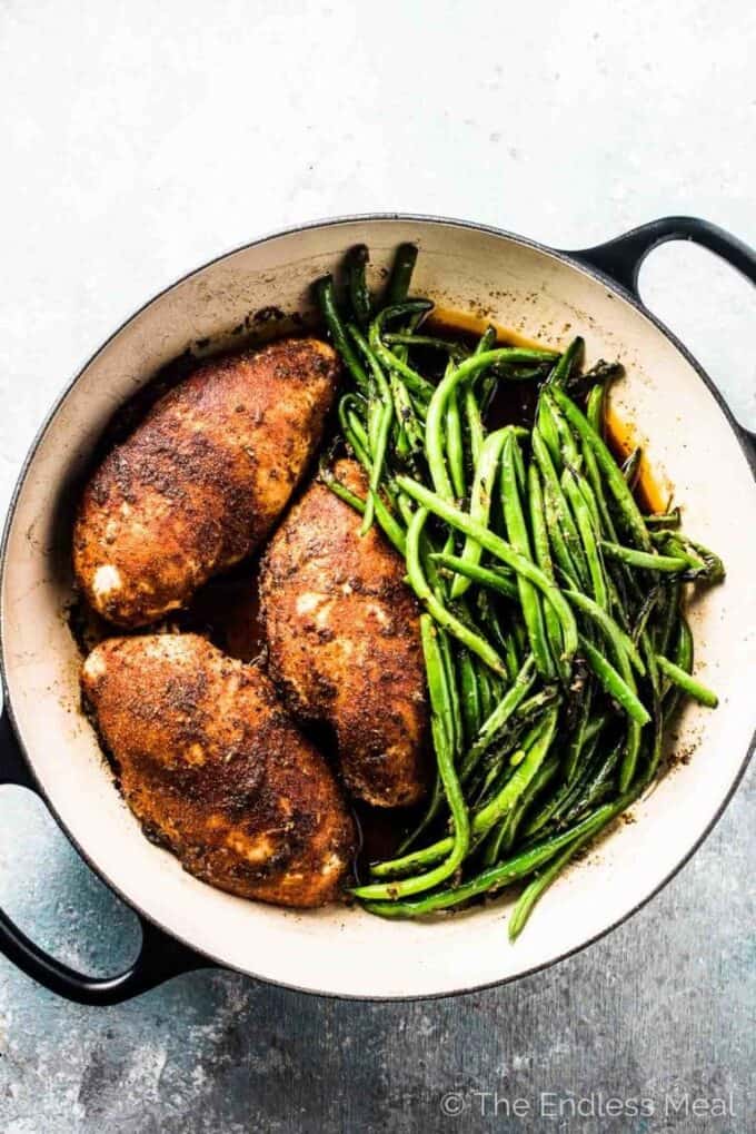 3 juicy oven baked chicken breasts in a pan with green beans on the side.
