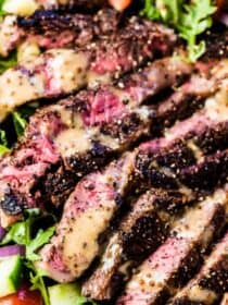 A close up of this steak salad with perfectly cooked sliced steak on top of veggies with some creamy balsamic dressing over the top.