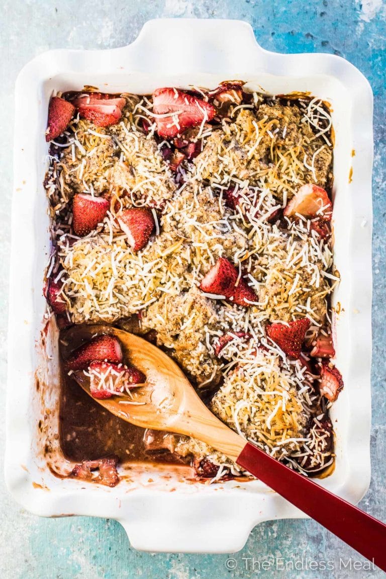 Healthy gluten-free strawberry rhubarb crisp on a blue table with a spoon in it.
