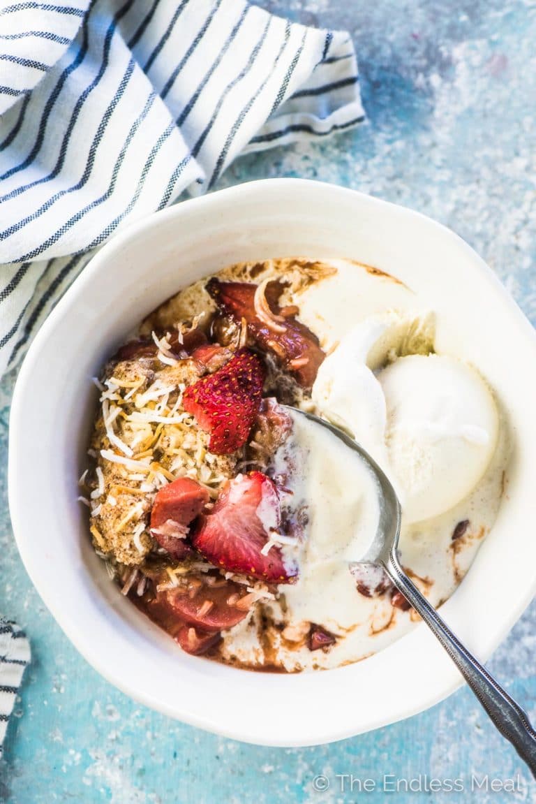 Healthy strawberry rhubarb crisp in a white bowl with vegan vanilla ice cream.