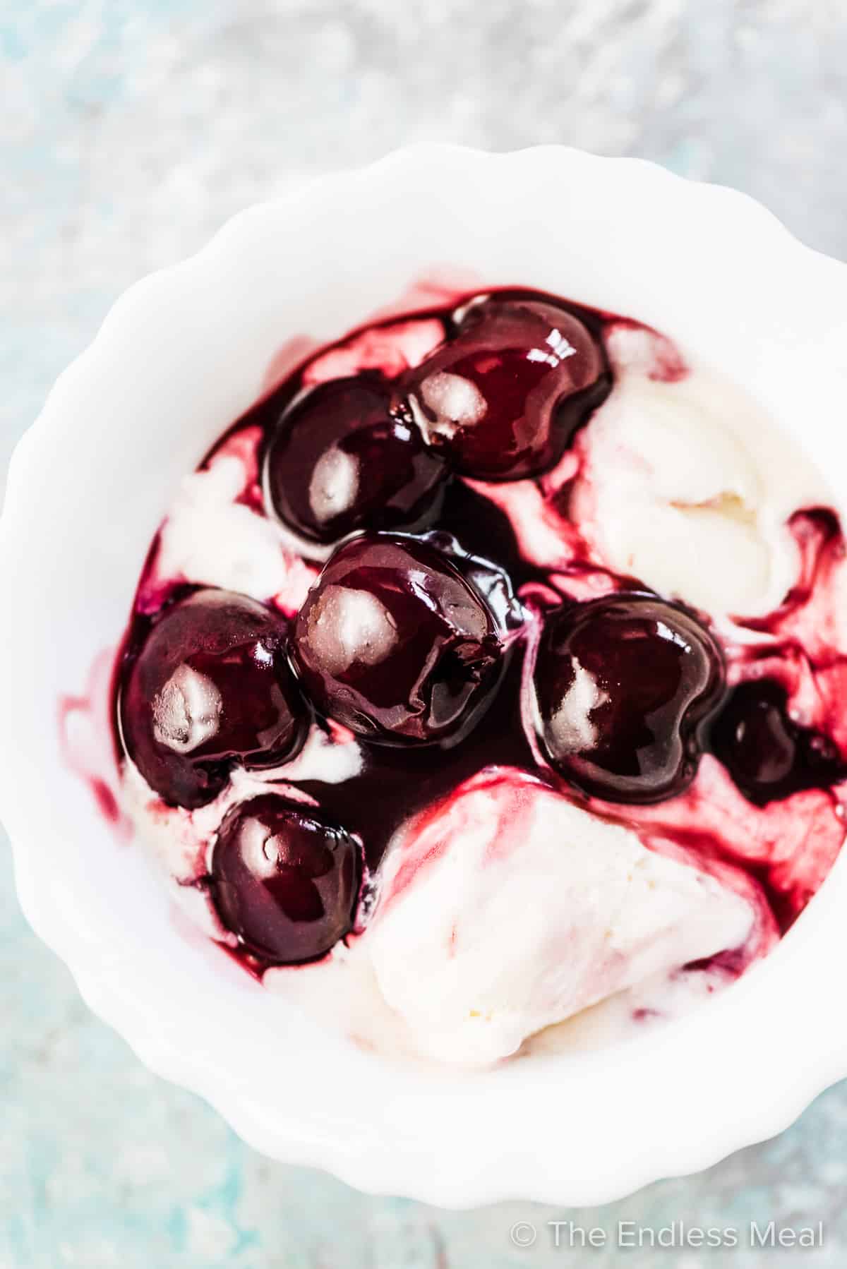 Fresh cherry sauce over a bowl of melting vanilla ice cream in a white bowl. 
