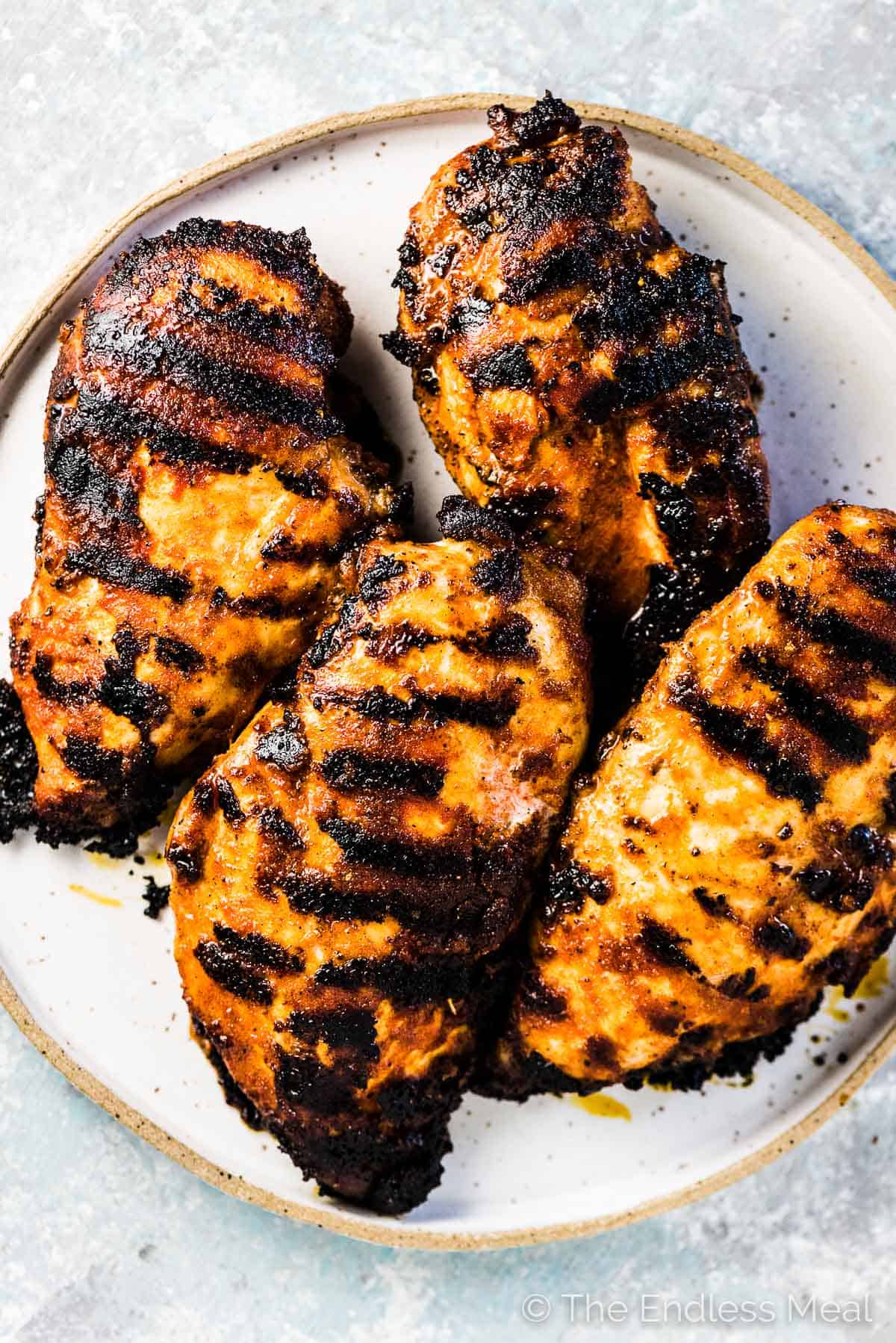 4 grilled chicken breasts with lots of tasty grill marks on a white plate.
