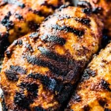 4 juicy grilled chicken breast on a plate with tasty grill marks all over them.