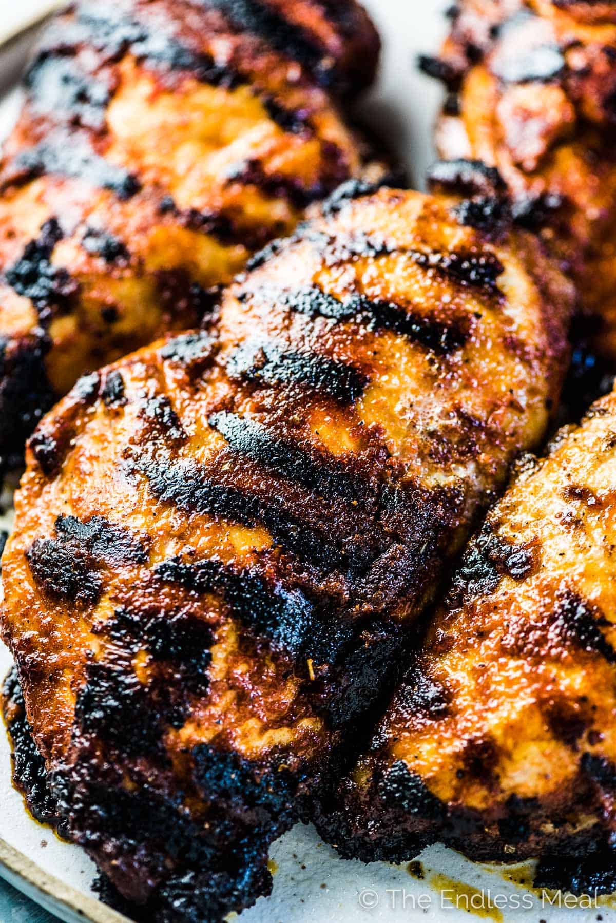 4 juicy grilled chicken breast on a plate with tasty grill marks all over them.