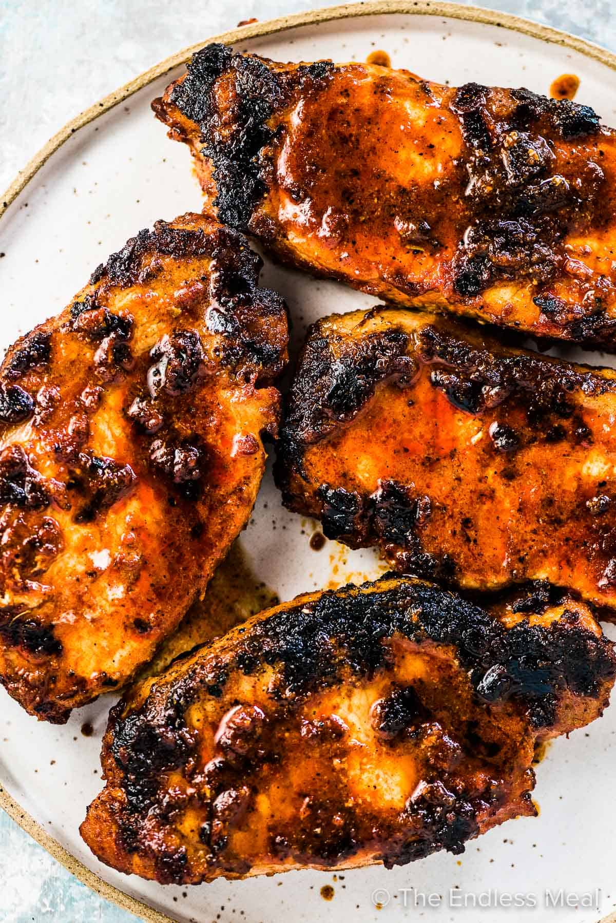 4 grilled pork chops with lots of tasty charred bits on a plate. 