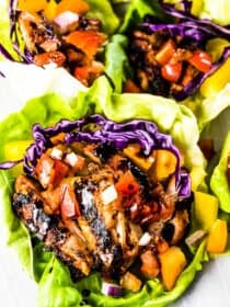 Three bruschetta chicken lettuce wraps on a plate with balsamic vinegar drizzled over the top.