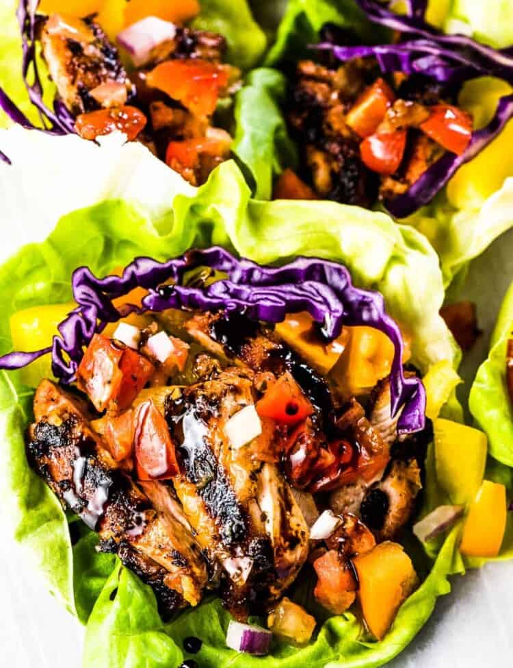 Three bruschetta chicken lettuce wraps on a plate with balsamic vinegar drizzled over the top.