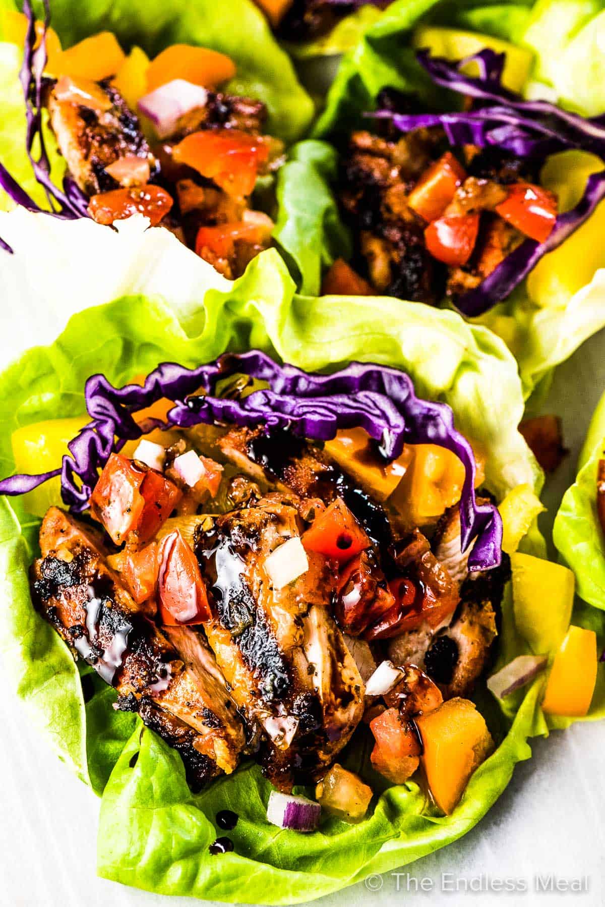 Three bruschetta chicken lettuce wraps on a plate with balsamic vinegar drizzled over the top. 