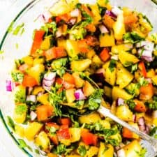 Fresh Peach Salsa in a glass mixing bowl and a spoon in the bowl.