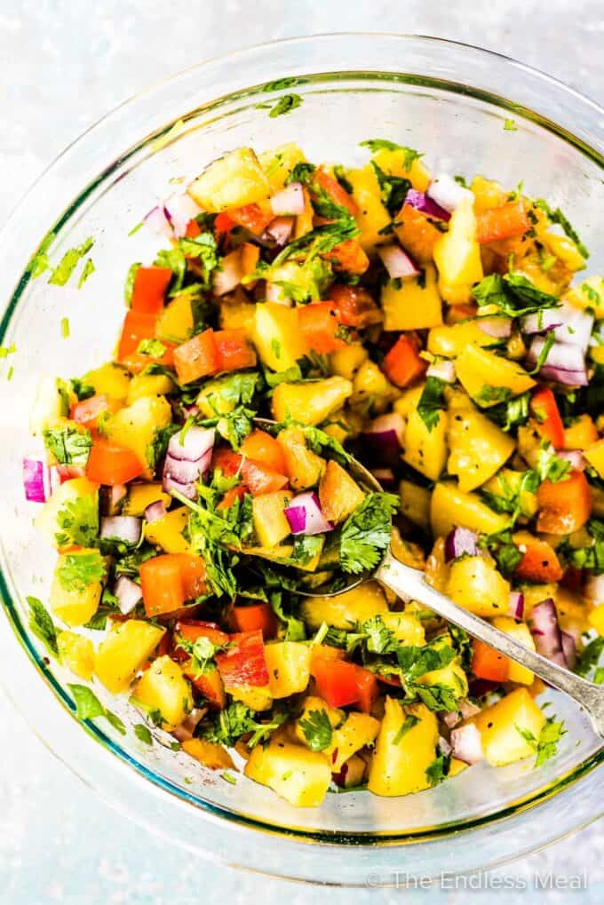 Fresh Peach Salsa in a glass mixing bowl and a spoon in the bowl.