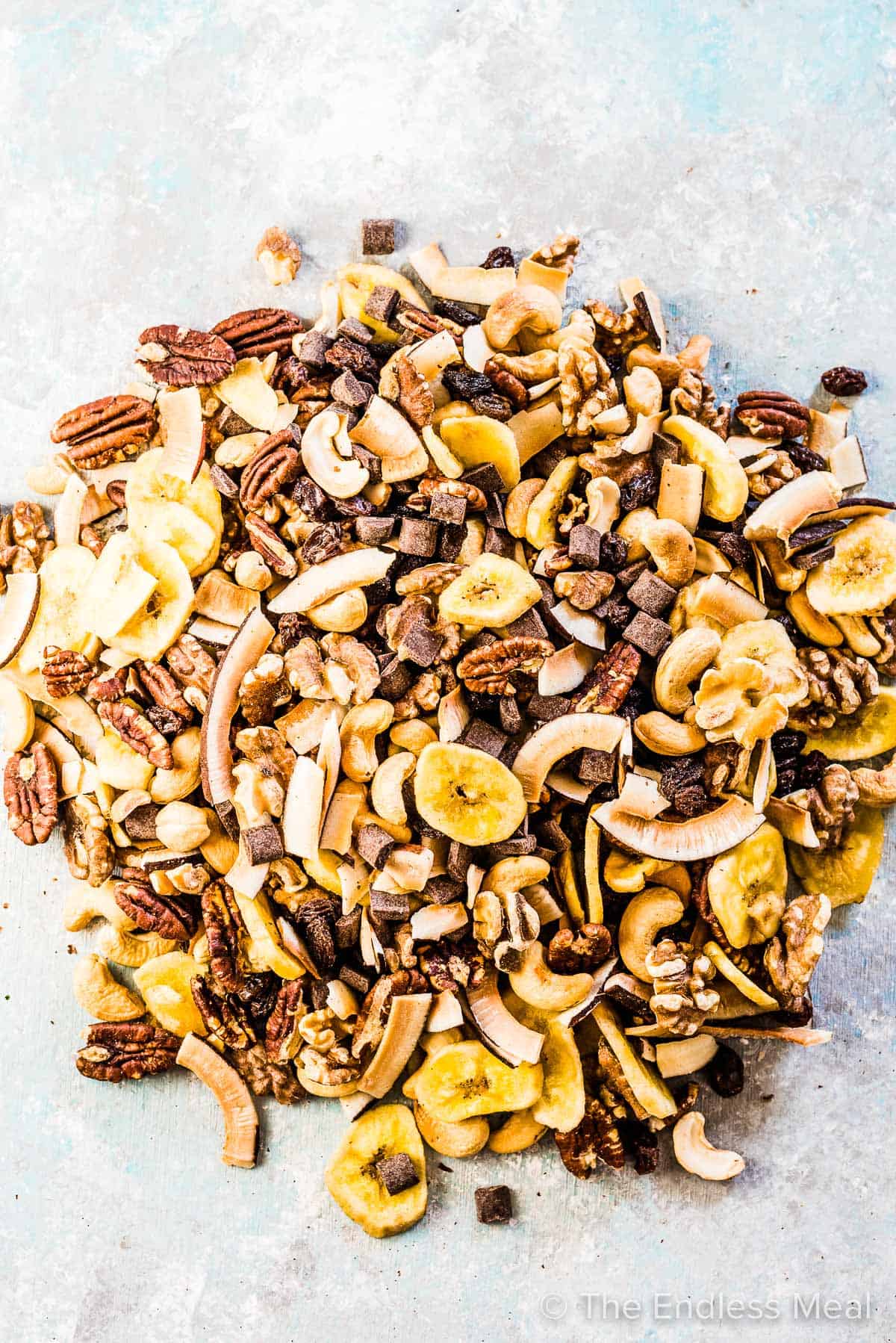 All the healthy trail mix ingredients mixed together on a blue board. 
