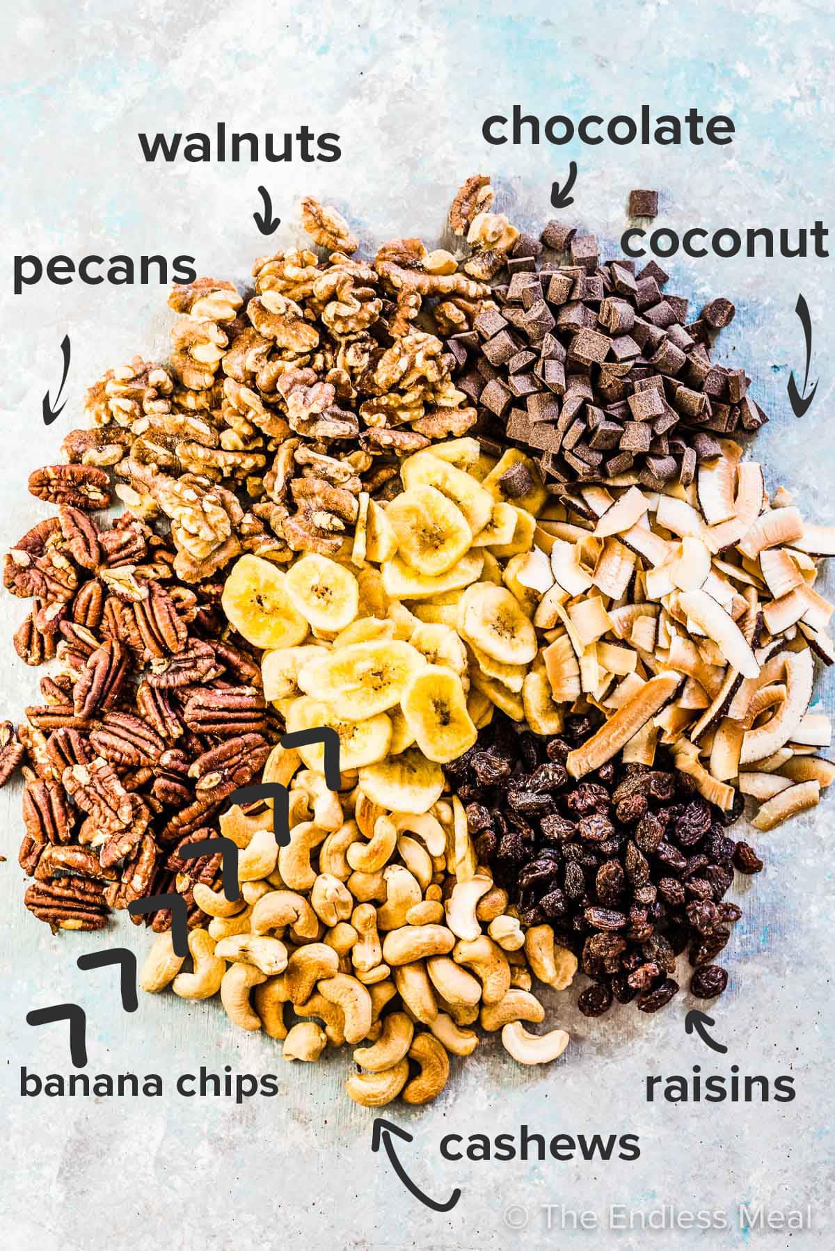 Homemade trail mix ingredients laid out on a blue board with the ingredient titles on the picture.