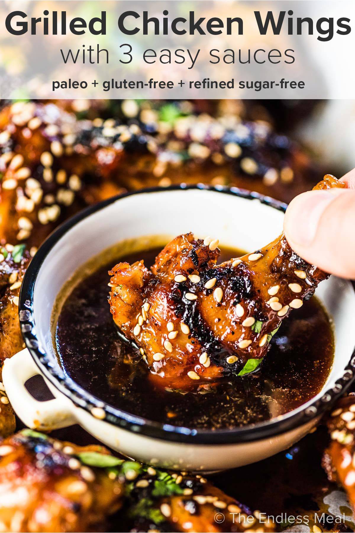 A grilled chicken wing being dipped into sticky sauce with the recipe title at the top of the picture. 