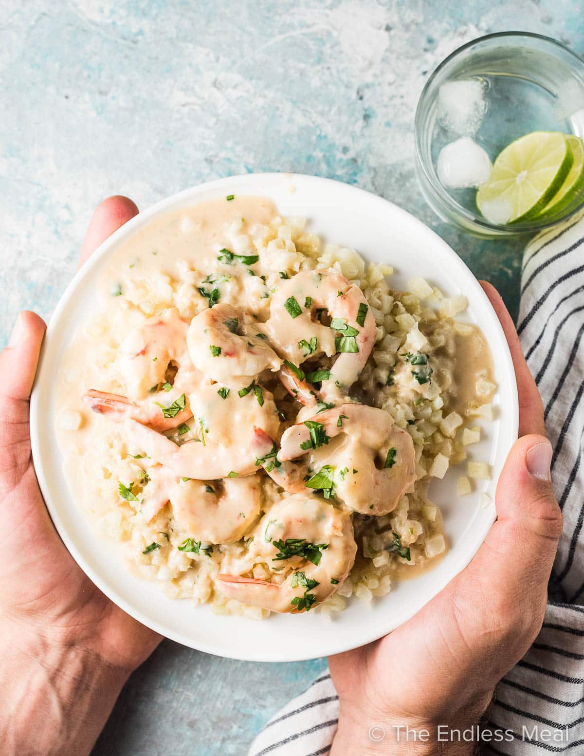 Hands holding a plate of coconut lime shrimp with cauliflower rice.