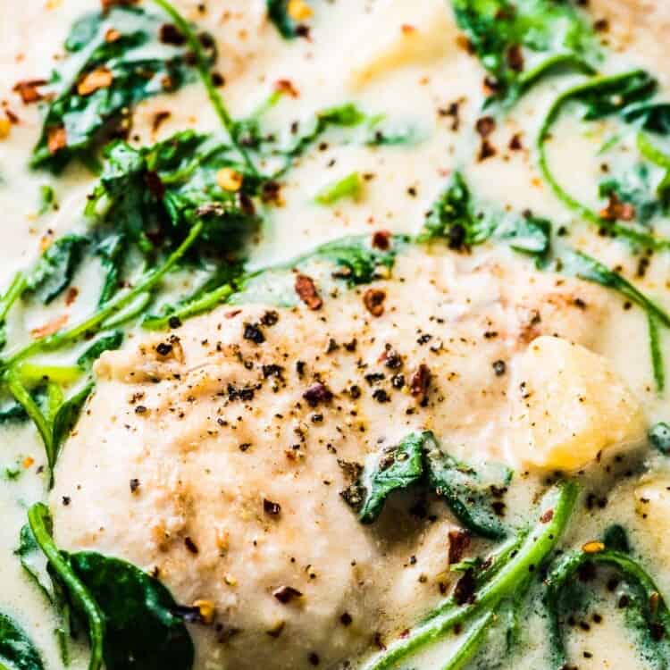A close up of creamy garlic chicken in a pan with lots of wilted spinach and cream sauce.